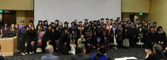 Group photo of graduates in their academic attire in front of the auditorium. 