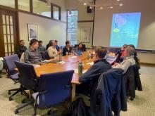 A group of people in conversation around an oval-shaped table.