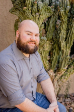 Man with beard wearing a grey shirt sits looking at the camera.