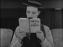 Black and white photo of man reading a book titled 'How to be a detective'.