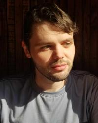 A headshot of a man with brown hair. The sun is shining onto his face.