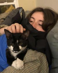 Woman looking down at a cat sitting on her black and blue vest.