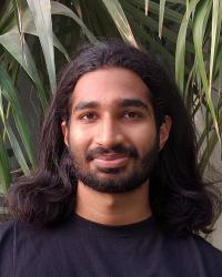 Man with shoulder length hair wearing black tshirt looks straight into camera.