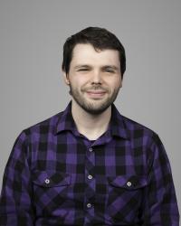 Headshot of Cain Miller. He is wearing a purple flannel and is against a grey backdrop.