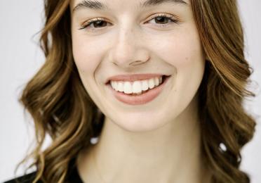 A young woman smiling, wearing a black t-shirt and gold necklace.