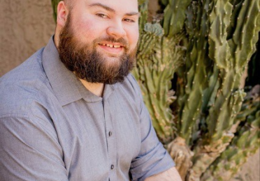 Man with beard wearing a grey shirt sits looking at the camera.