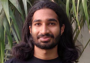 Man with shoulder length hair wearing black tshirt looks straight into camera.