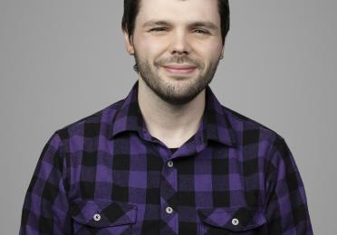 Headshot of Cain Miller. He is wearing a purple flannel and is against a grey backdrop.