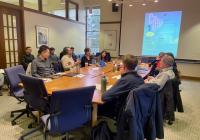 A group of people in conversation around an oval-shaped table.