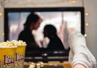 Person watching a movie at home, with a popcorn container on the table and stockinged feet resting on the edge of the table.