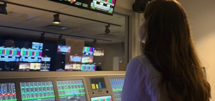 Woman looking up at TV monitor in front of broadcast switchboard