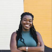 A woman smiling, her arms are crossed.