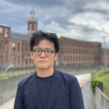 A young man, not smiling, wearing a black blazer.